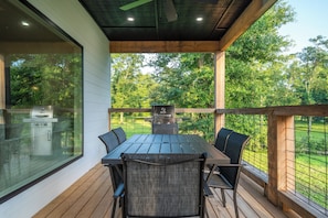 A covered outdoor dining area with a grill, a table, and chairs.