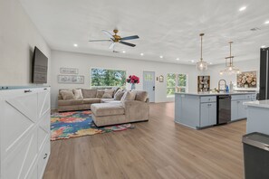 A spacious living area with a sofa, a coffee table, and a kitchen area with a dishwasher. - Lux Waterfront Cabin - 2 King Ensuites, Large Covered Porch, Kayaks, Fire Pit! (Royal)