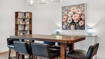 A dining area with a wooden table, four chairs, a bookshelf, and a floral painting on the wall.