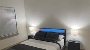 Un dormitorio con una cama, dos mesitas de noche, un ventilador de techo y una ventana con persianas.