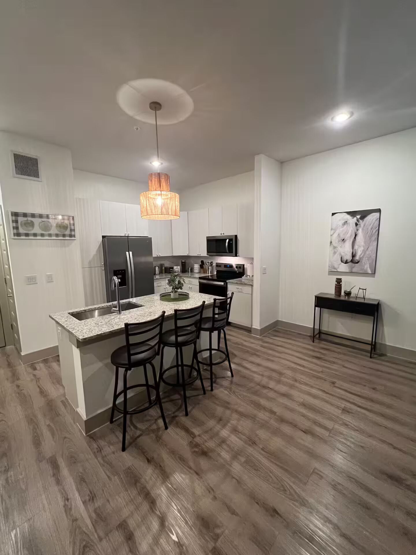 A modern kitchen with a central island, bar stools, stainless steel appliances, and a pendant light.