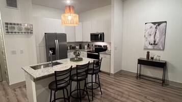 A modern kitchen with a central island, bar stools, stainless steel appliances, and a pendant light.