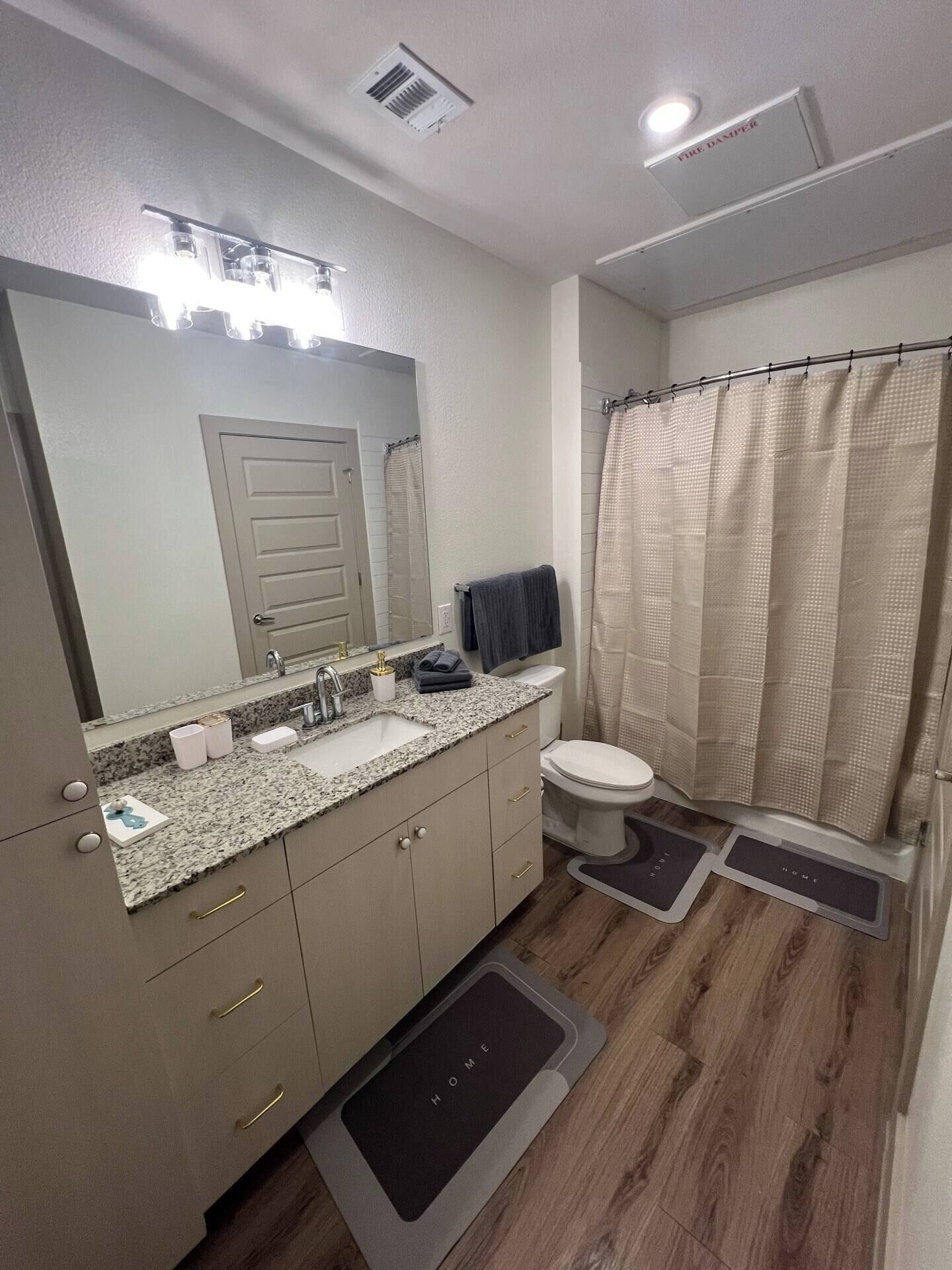 A bathroom with a sink, mirror, toilet, shower curtain, and a rug with 'HOME' on it.