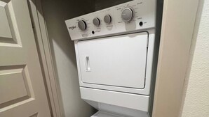 Una lavadora y secadora Whirlpool blancas, compactas, instaladas en un cuarto de lavado pequeño y cerrado con una puerta a la izquierda.