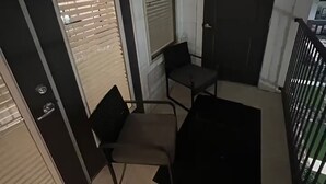 Un balcón con una silla, una mesita y una puerta con ventanal.