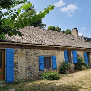 A stone building with a tiled roof, blue shutters, and a small window. - La Bergerie de Louisa (sleeps 4–5) (MARVEJOLS)