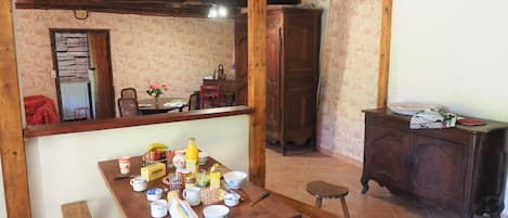 Ein Essbereich mit einem Holztisch, gedeckt für das Frühstück, einer Bank und einem Schrank mit diversen Gegenständen.