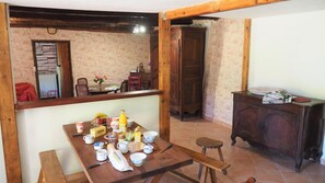 A dining area with a wooden table set for breakfast, a bench, and a cabinet with various items. - La Bergerie de Louisa (sleeps 4–5) (MARVEJOLS)