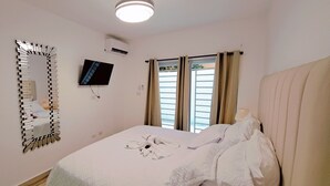 A hotel room with a bed, a television mounted on the wall, an air conditioning unit, and a window with curtains. - COSTA DE LUXE (Bayahíbe)