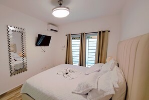 Ein Hotelzimmer mit Bett, einem an der Wand montierten Fernseher, einer Klimaanlage und einem Fenster mit Vorhängen.