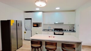 A modern kitchen with white cabinets, a central island with stools, a refrigerator, a microwave, and a stove. - COSTA DE LUXE (Bayahíbe)
