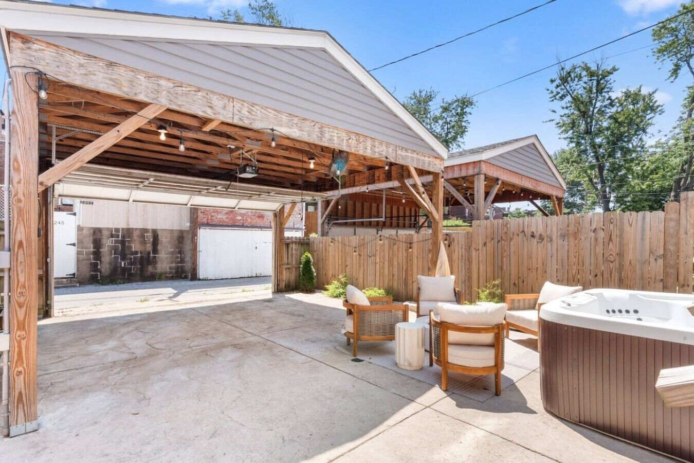 A covered outdoor area with a hot tub, seating, and a garage.