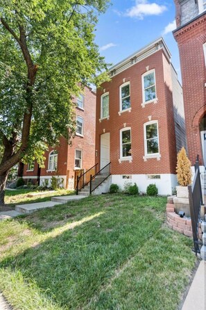 A two-story brick building with a front entrance, a small front yard, and a tree to the left. - The Jefferson Social | Sleeps 12 | Pool Table (St. Louis)