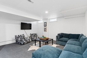 A modern living room with a large sofa, a smaller sofa, a coffee table, and a flat-screen TV mounted on the wall. - The Jefferson Social | Sleeps 12 | Pool Table (St. Louis)