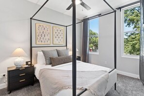 A four-poster bed with a canopy, a bedside table with a lamp, and two framed floral artworks on the wall.