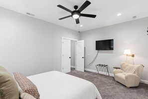 A bedroom with a bed, a ceiling fan, a TV, a lamp, and a chair. - The Jefferson Social | Sleeps 12 | Pool Table (St. Louis)
