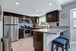 Eine moderne Küche mit Edelstahlgeräten, dunklen Holzschränken, Granit-Arbeitsplatten und einer eingebauten Kochinsel mit Barhocker.