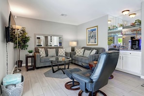 A living room with a sofa set, a coffee table, a leather chair, a TV mounted on the wall, and a bar area with shelves. - Desert Retreat with Private Pool & Spa | Near Downtown Palm Springs (Palm Springs)