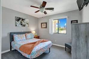 A bedroom with a bed, a ceiling fan, a window with a view, and artwork on the walls. - Desert Retreat with Private Pool & Spa | Near Downtown Palm Springs (Palm Springs)