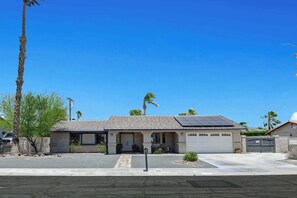 Une maison d’habitation avec un garage, des panneaux solaires et un ciel bleu dégagé.