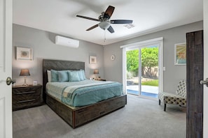 Ein Schlafzimmer mit einem Bett, Nachttischen, einem Deckenventilator und Blick durch eine Schiebetür.