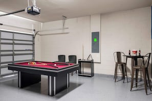 A pool table with a red felt surface, two black chairs, a table with bottles, and a projector mounted on the ceiling. - Disney Escape . Family Retreat . Private Pool (Davenport)
