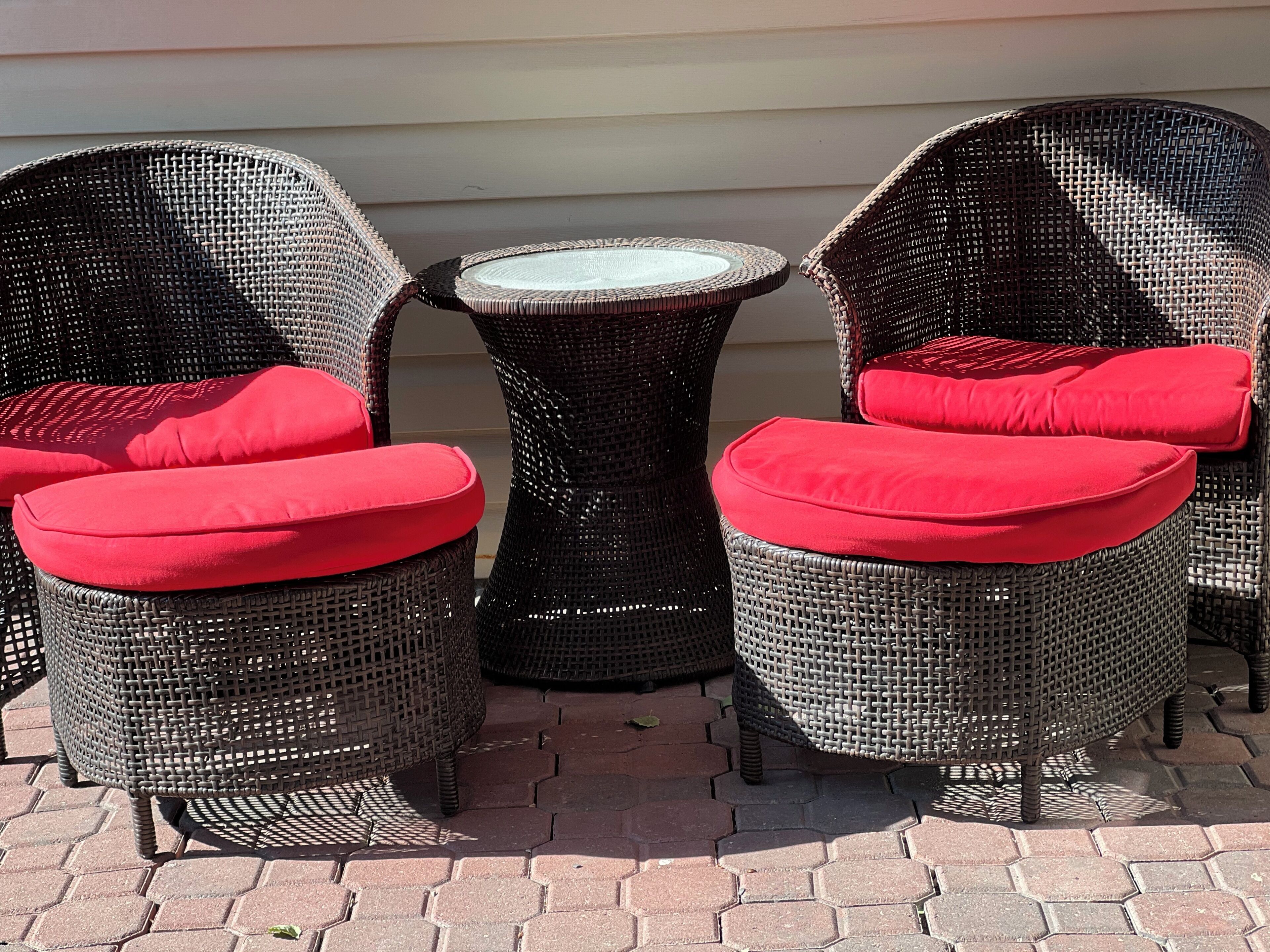 A set of wicker chairs with red cushions and a small round table, placed on a paved patio.