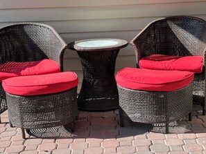 Et sæt fletstole med røde puder og et lille rundt bord, placeret på en anlagt terrasse.