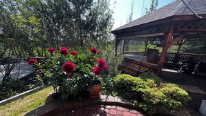 En have med et brobelagt sti, en træpergola og en potteplante med røde blomster.