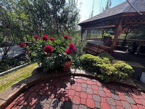 Ein Gartenbereich mit einem Pflasterweg, einer Holz-Pergola und einem Blumentopf mit roten Blüten.