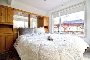 A bedroom with a large bed, wooden wardrobe, and a window with a view of a gazebo. - NW Calgary Walkout Basement Furnished  1bedroom 1 bathroom Parking (Calgary)