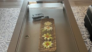Et sofabord med glasplade, en vævet bakke og to fjernbetjeninger.