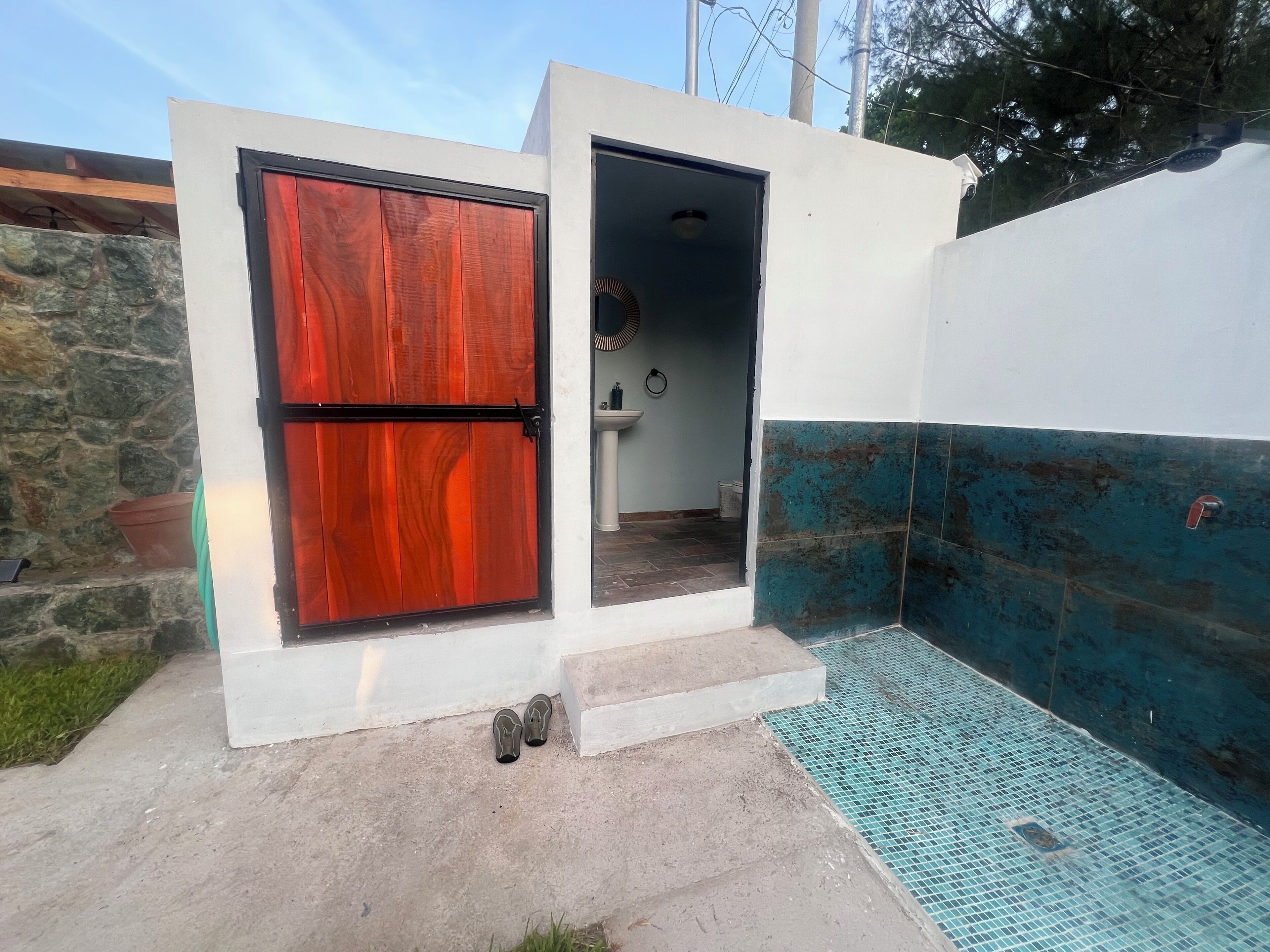 Un petit espace extérieur clos, doté d’une porte en bois, d’un sol carrelé et d’un mur recouvert de carreaux bleus.