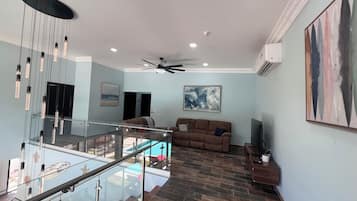 Uma sala de estar espaçosa, com guarda-corpo de vidro, um sofá marrom e um ventilador de teto.