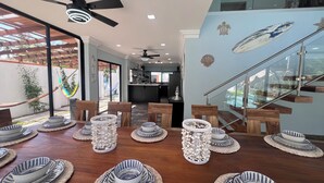 A dining area with a wooden table set for a meal, a ceiling fan, and a view of the kitchen and living space. - Paradise found on Costa Azul, sleeps 12 in 5 bedrooms. One minute to the beach (Acajutla)