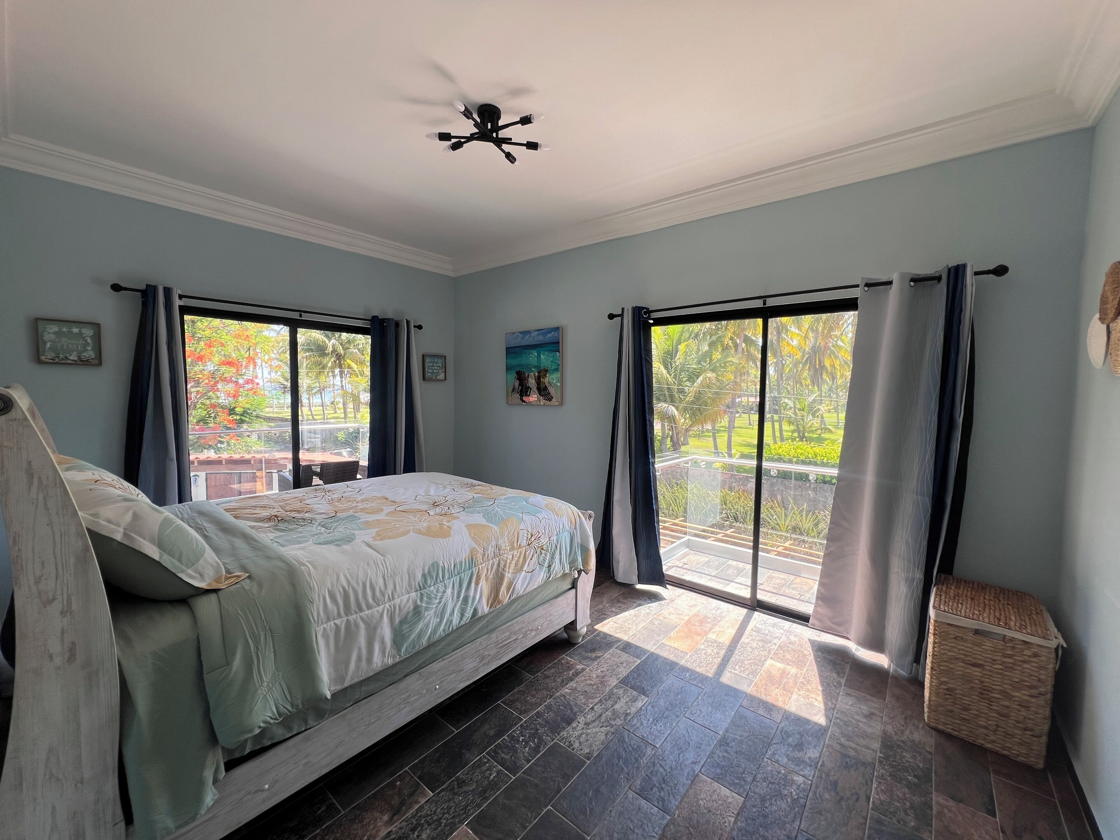 Un dormitorio con cama, ventilador de techo y vista a un jardín por un ventanal corredero.