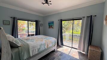 Un dormitorio con cama, ventilador de techo y vista a un jardín por un ventanal corredero.