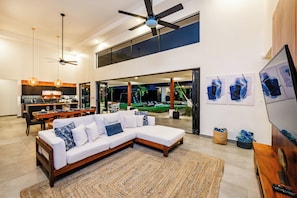 A modern living room with a sectional sofa, a dining area, and a view of the outdoor space. - 4-Bedroom House with Pool at Hacienda Pinilla (Pinilla)