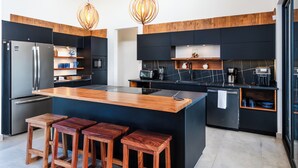 Une cuisine moderne dotée d’un îlot central, de tabourets de bar, d’appareils électroménagers en acier inoxydable et d’éléments décoratifs en bois.