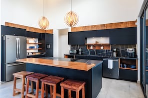 A modern kitchen with a central island, bar stools, stainless steel appliances, and wooden accents. - 4-Bedroom House with Pool at Hacienda Pinilla (Pinilla)