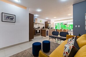 A modern living room with a sofa, ottomans, and a dining area with chairs and a table. - Stylish 3BR Stay • Roma Norte, Balcony & Workspace (Ciudad de México)