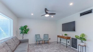 Un salon comprenant un canapé, deux fauteuils à motifs, une table basse, un téléviseur et un ventilateur de plafond.