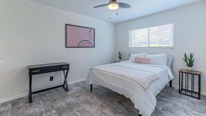 Une chambre à coucher avec un lit, un bureau, un ventilateur de plafond, une fenêtre et une plante en pot.