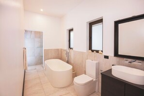 Un baño moderno con una bañera independiente, un inodoro y un tocador con un espejo grande.