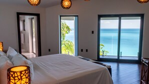 Un dormitorio con una cama grande, dos puertas que dan a un balcón con vistas al mar y una lámpara colgante.