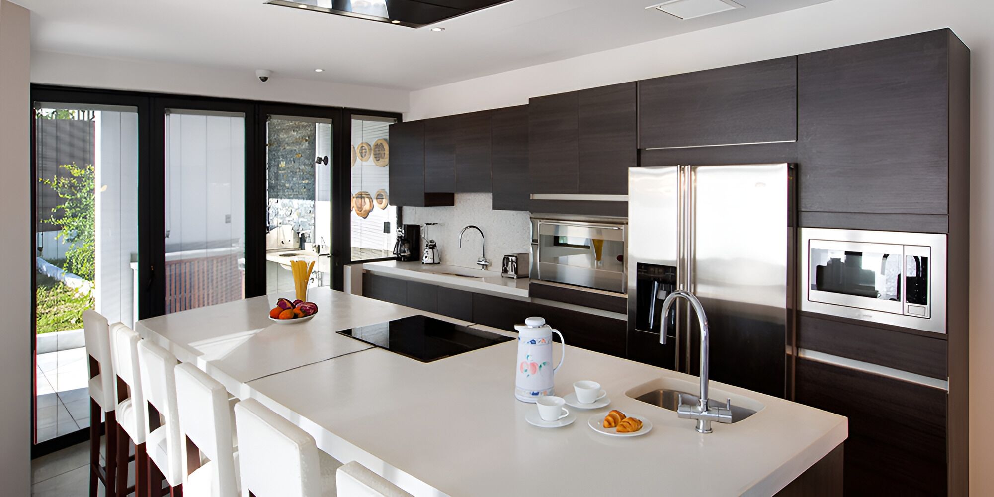 A modern kitchen with a central island, stainless steel appliances, and a large window overlooking a balcony.