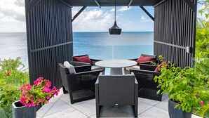 Un espacio de estar al aire libre cubierto con vistas al mar, con mobiliario de mimbre y plantas en macetas.