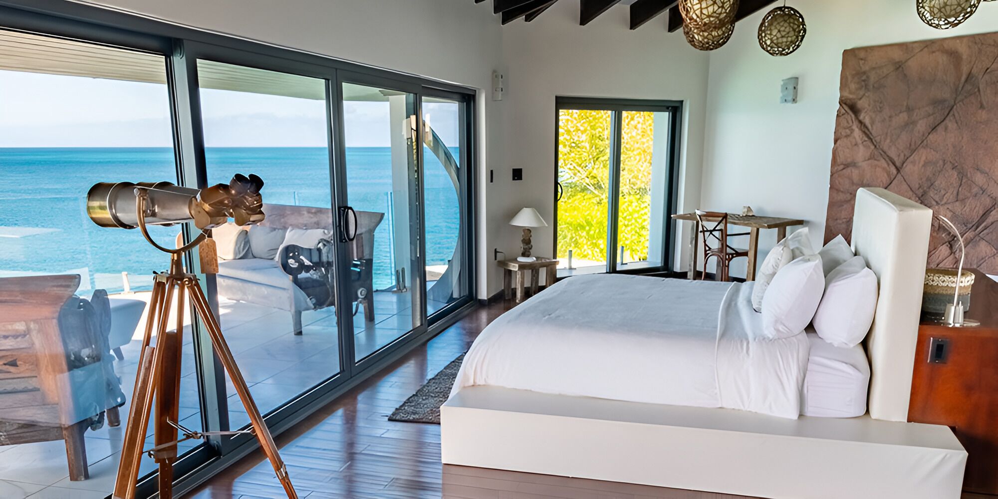 A bedroom with a large bed, a telescope, and a view of the ocean.