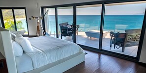 Un dormitorio con una cama grande, un telescopio y vistas al océano a través de ventanas de piso a techo.