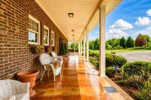 A covered porch with wicker furniture and potted plants, leading to a brick building.